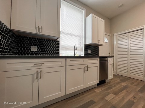 A kitchen with white cabinets and a black and white tiled backsplash.