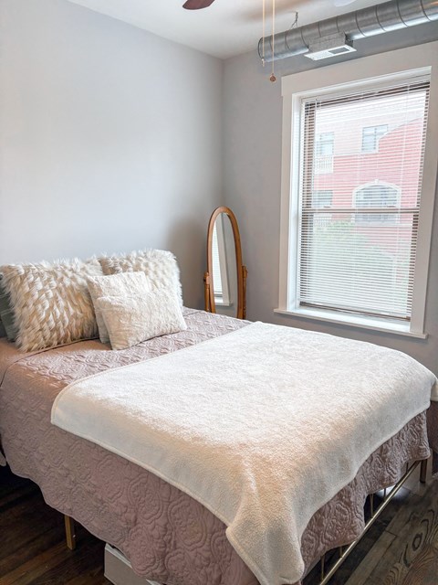 A bed with a white comforter and a pillow with a white pillow case sits in a bedroom.