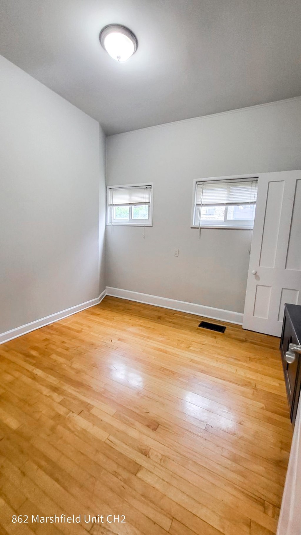 A room with wooden flooring and two windows.