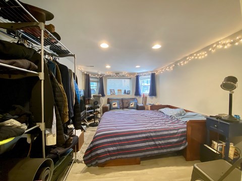 A bedroom with a bed, a clothing rack, and a window with curtains.