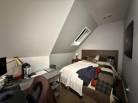 A bedroom with a bed, desk, chair, and a lamp.
