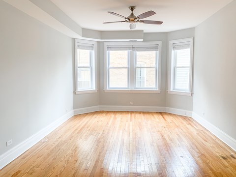A room with a ceiling fan and three windows.