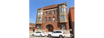 Two white cars are parked in front of a red brick building.