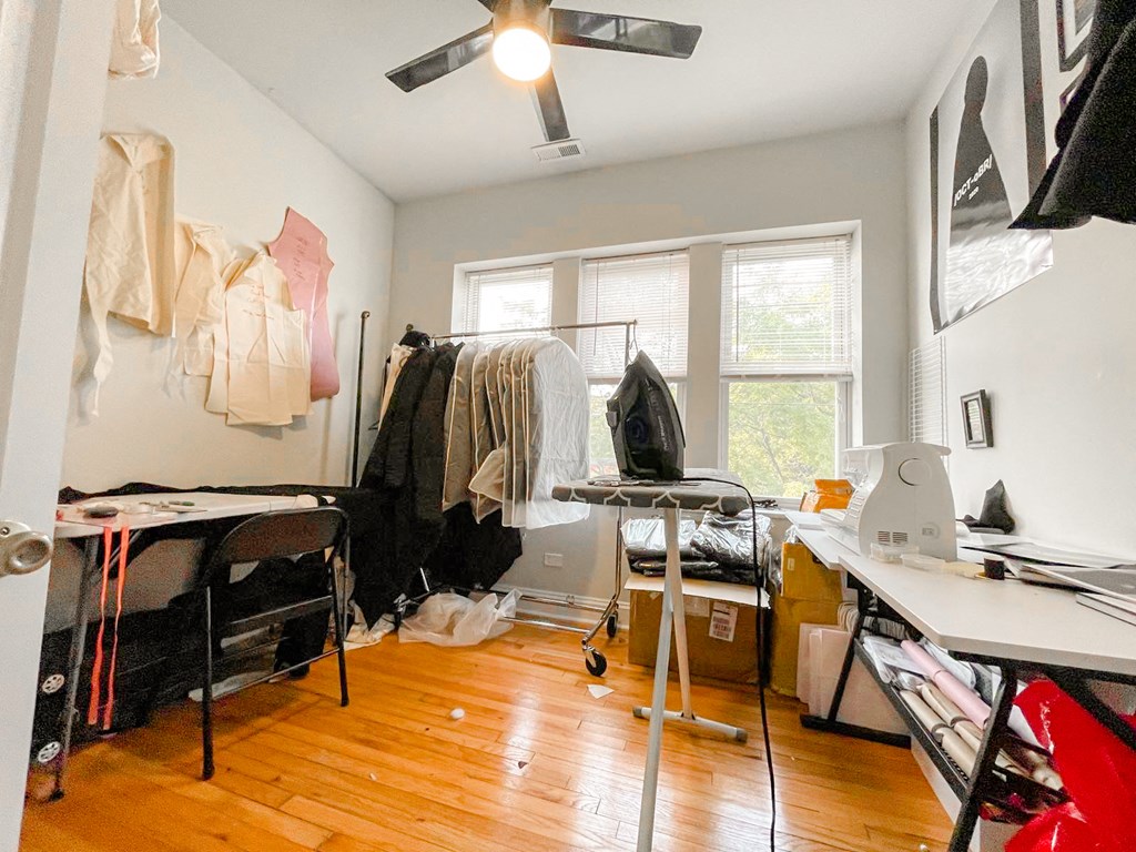 a bedroom with a desk and clothes hanging on the wall and a window