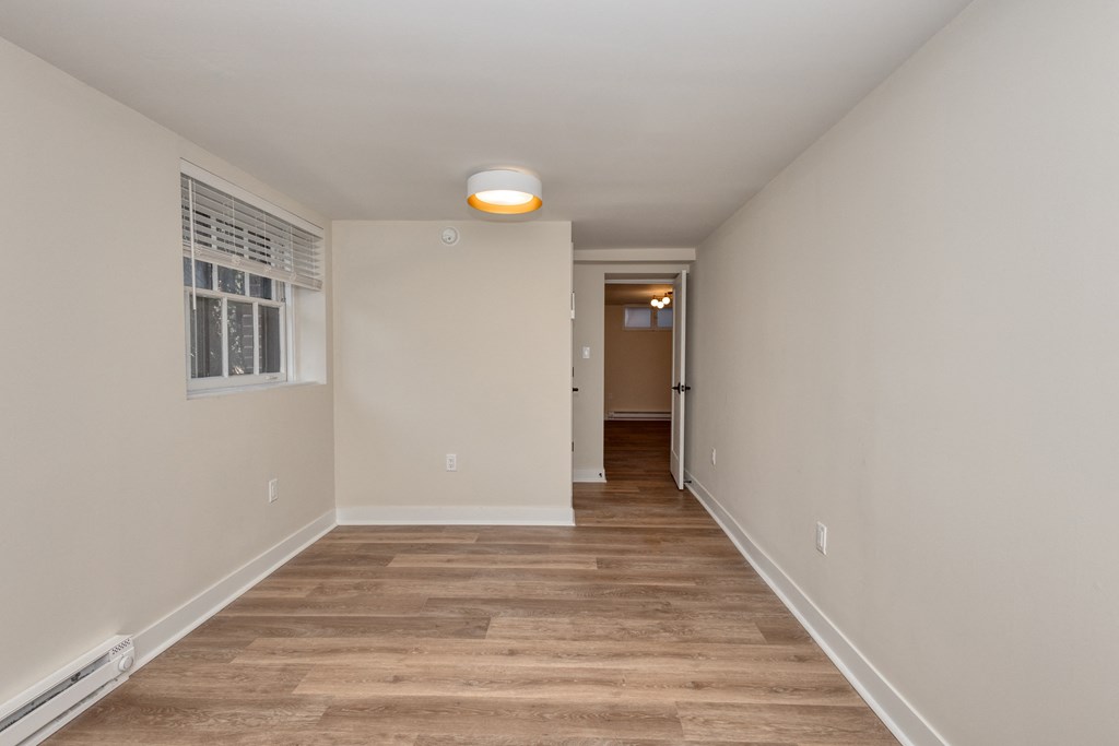 a long hallway with white walls and wood flooring and a window