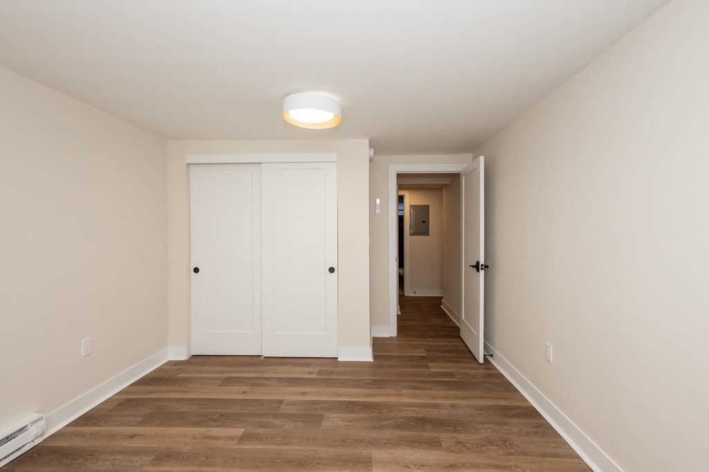 a long hallway with wood flooring and white walls and a door to a closet