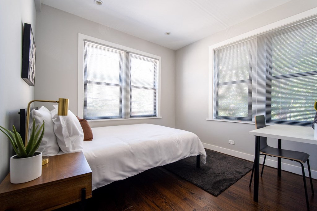 a bedroom with a bed and a desk and two windows