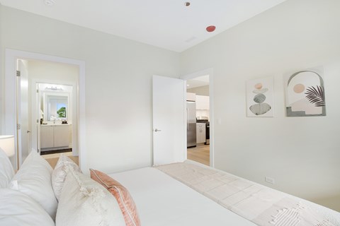 A white bedroom with a bed and a painting on the wall.