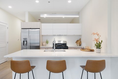 A modern kitchen with white countertops and brown chairs.