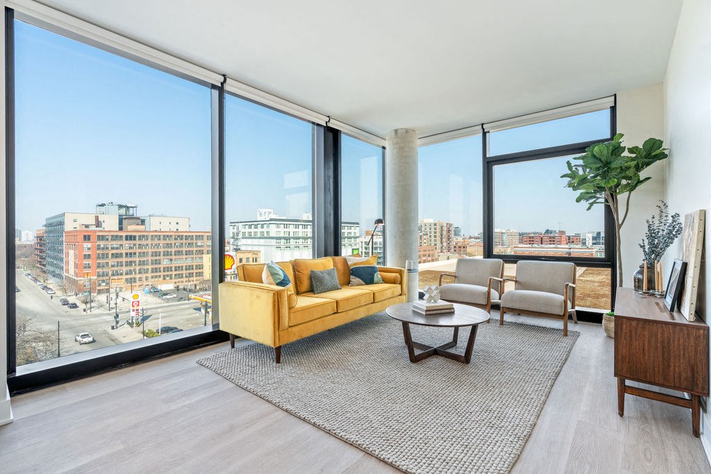 a living room with large floor to ceiling windows and and wide plank flooring and a couch and two living room chairs