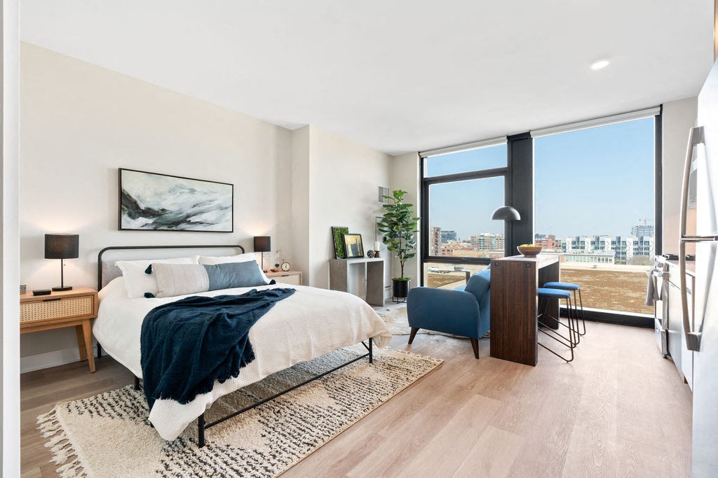 a studio apartment with wide plank flooring a bed and a couch and floor to ceiling windows