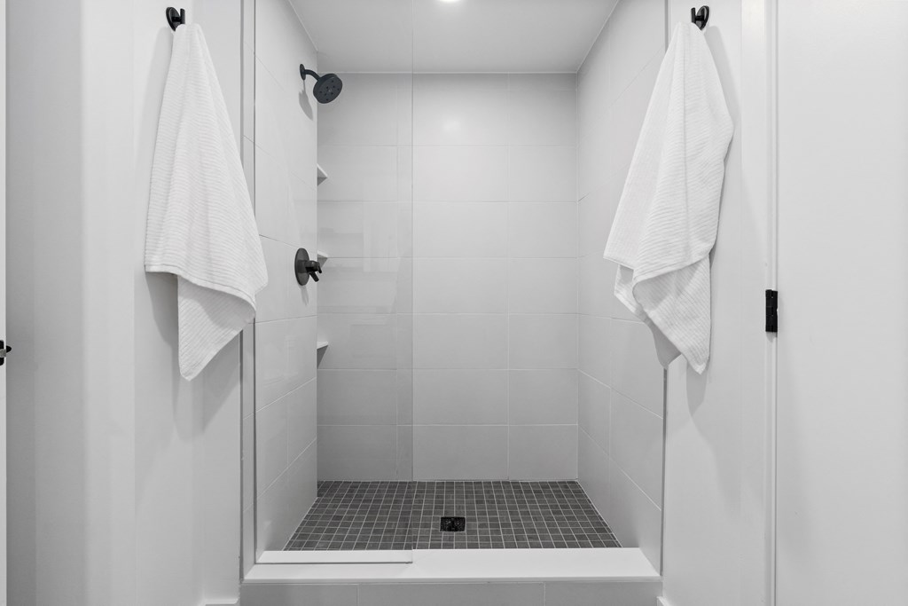 a white bathroom with two white towels hanging in a shower