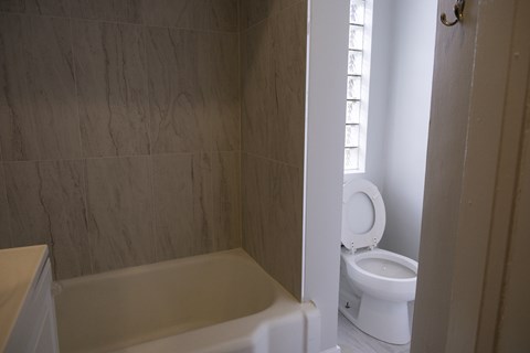 A white toilet is in a bathroom with a white tub.