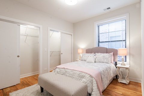 A bedroom with a bed, two lamps, and a window with blinds.