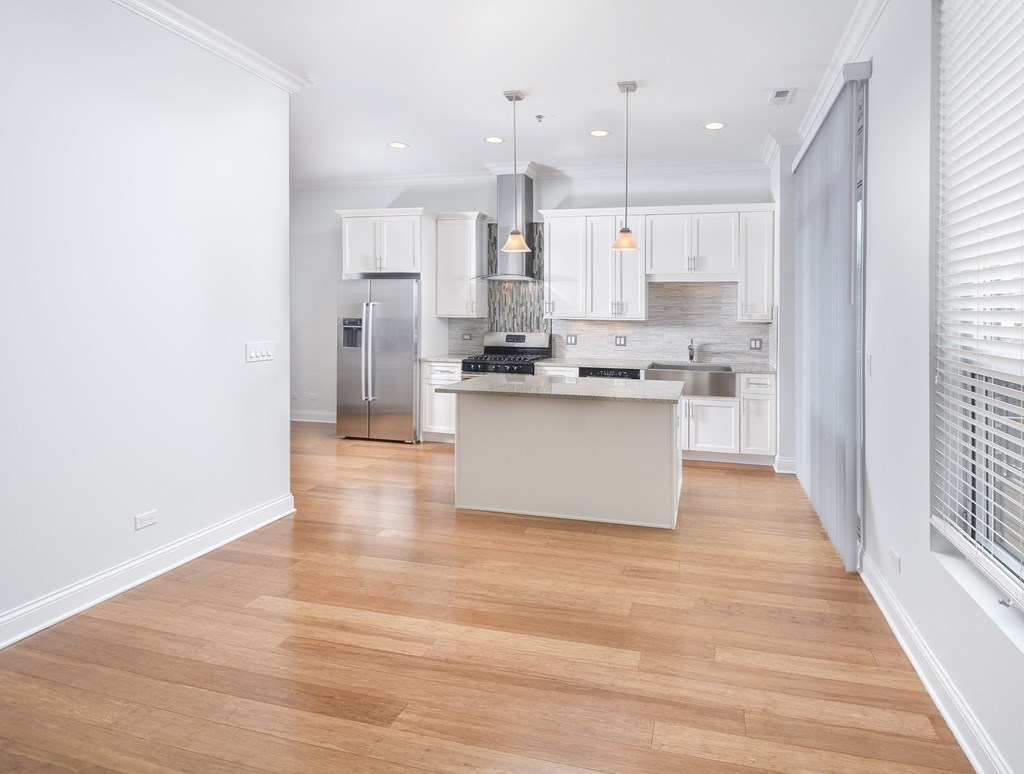 a living room with a kitchen with white cabinets and a wood floor