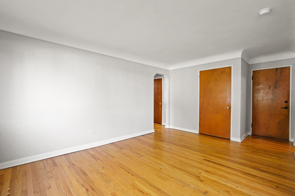 a living room with white walls and wooden floors and two doors