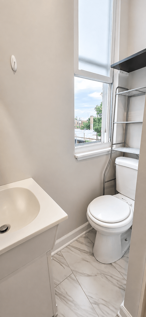 A white toilet in a bathroom with a sink and a window.