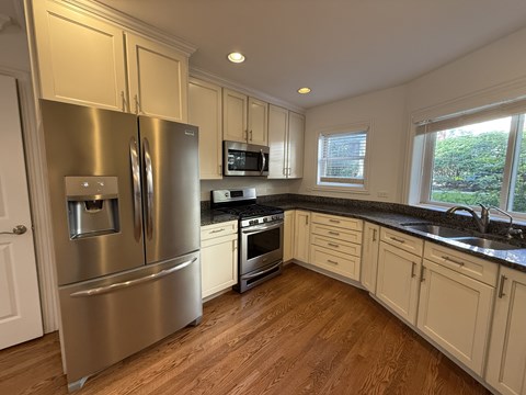 A kitchen with a stainless steel refrigerator and wooden floors.