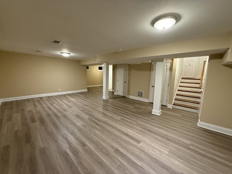 A room with wooden flooring and a staircase in the background.
