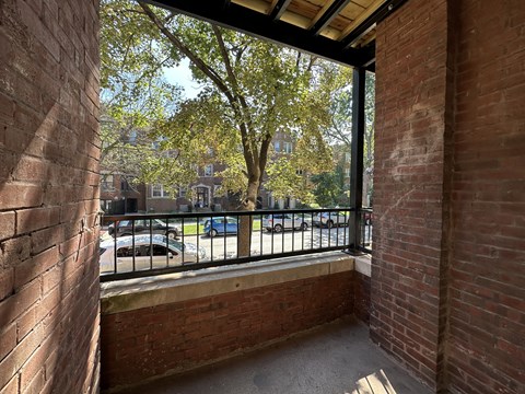 A balcony with a brick wall and a metal railing overlooking a parking lot.