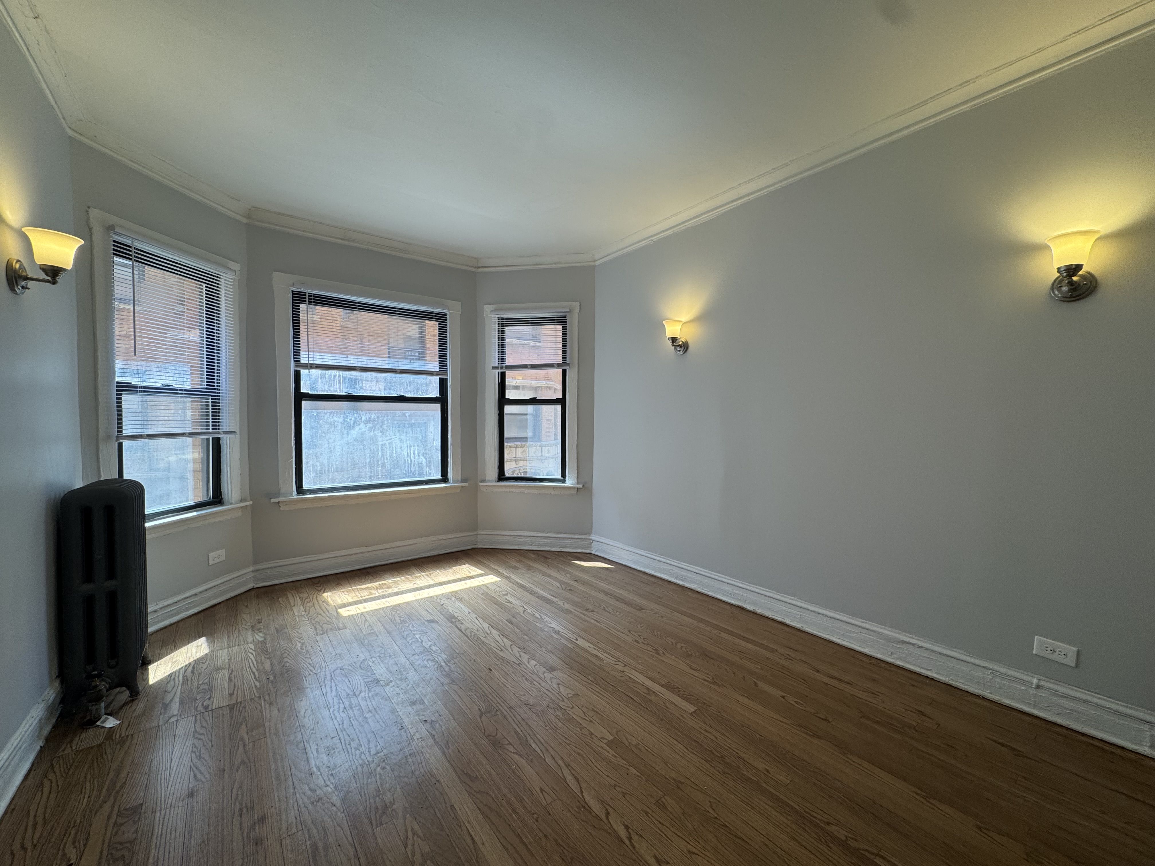 A room with wooden floors and three windows.