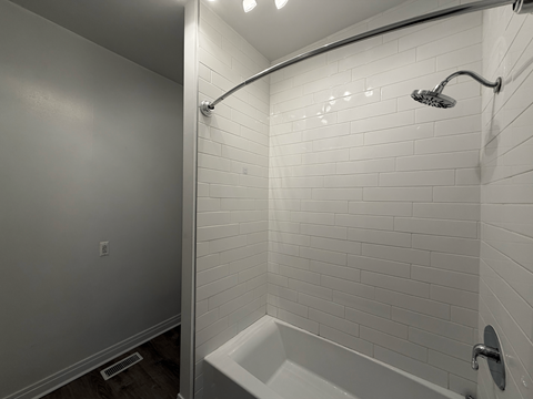 A white tiled bathroom with a white tub and shower head.