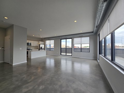 A large, empty room with a concrete floor and a kitchen area in the background.