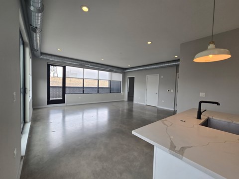 A large, empty room with a kitchen island and a window overlooking a construction site.