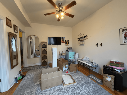 A room with a ceiling fan and boxes on the floor.