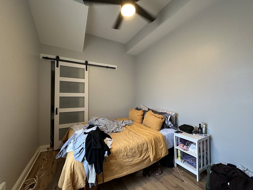 A bedroom with a bed, a ceiling fan, and a sliding door.