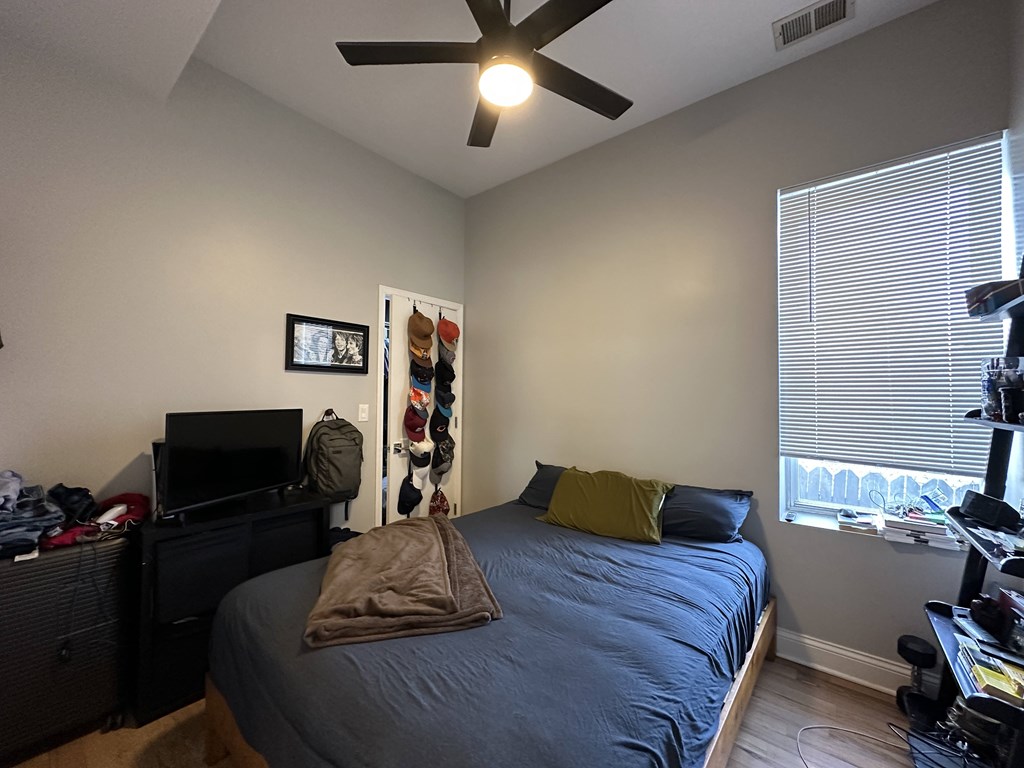 A bedroom with a bed, a ceiling fan, and a window with blinds.
