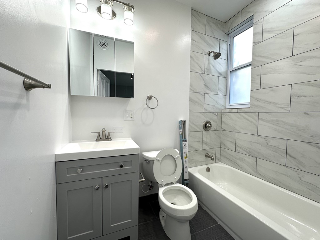 A white toilet sits in a bathroom with a white sink and a white bathtub.