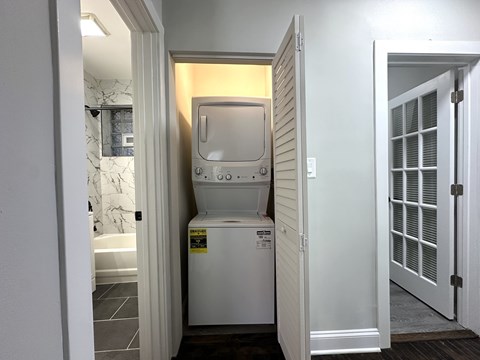 A small white washing machine is in a narrow space between two doors.