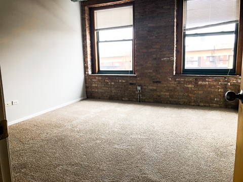 A room with a carpeted floor and two windows.