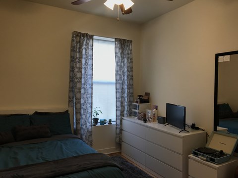 A bedroom with a bed, dresser, and window with curtains.