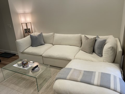A white couch with grey pillows and a glass coffee table in a living room.