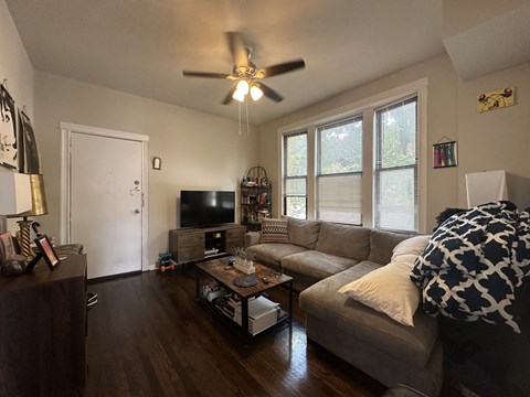 A living room with a couch, a television, and a ceiling fan.