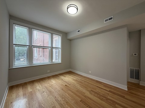 A room with wooden floors and a window showing a view of a red building outside.