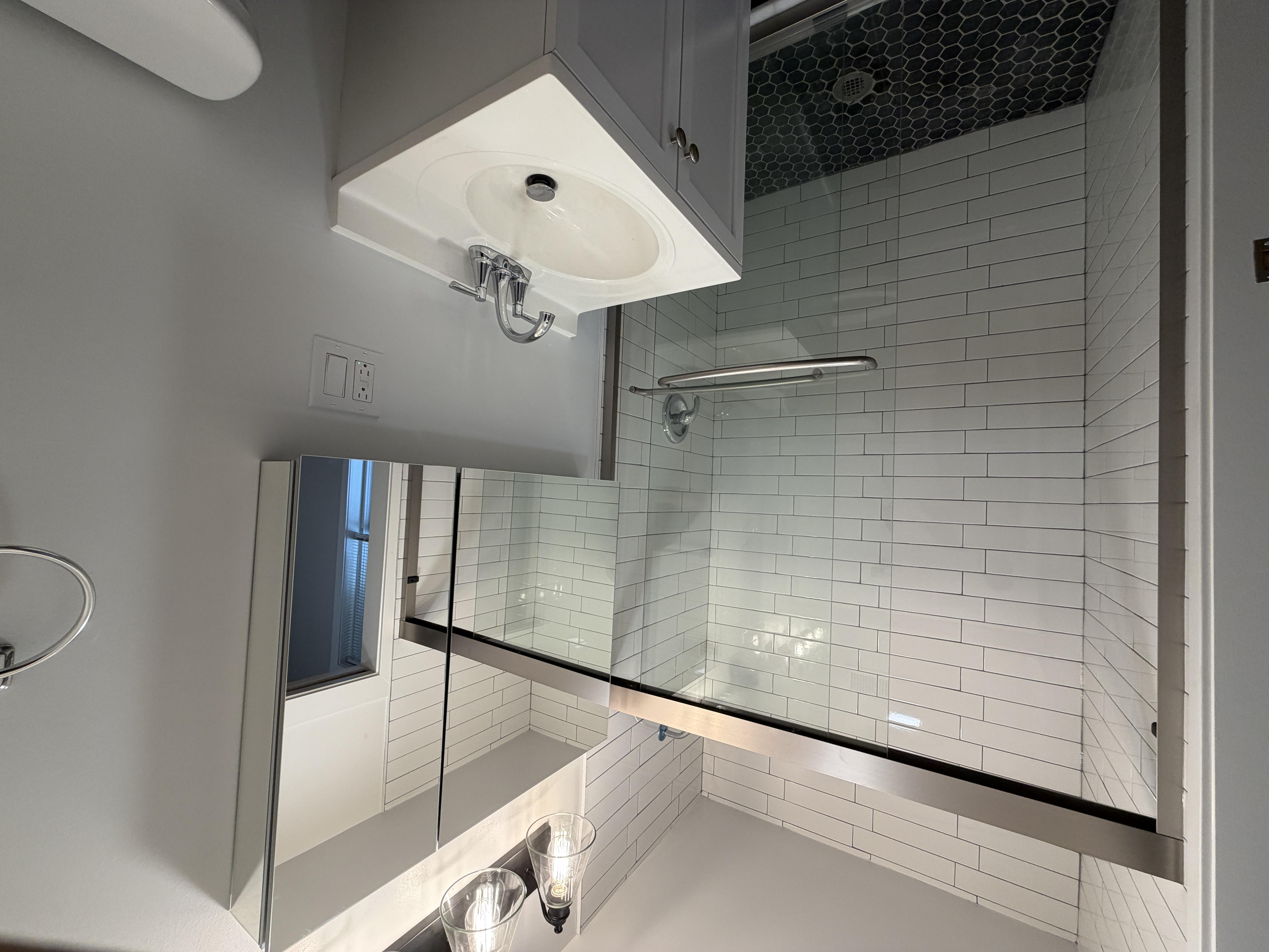 A modern bathroom with a glass shower enclosure and a white tiled wall.