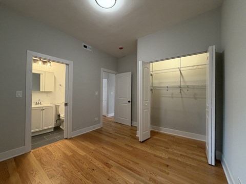 A room with a wooden floor and a white wall with a closet and a door.
