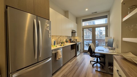 A modern kitchen with a stainless steel refrigerator and a desk with a computer.