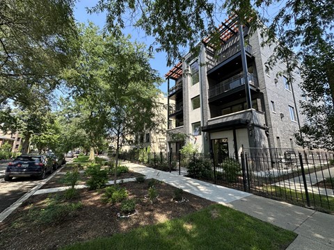 A modern building with a balcony is surrounded by trees and a black fence.