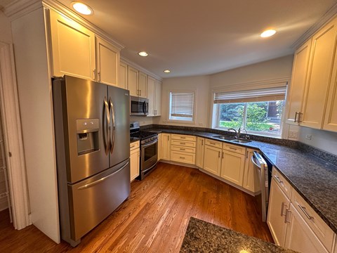 A kitchen with a stainless steel refrigerator and wooden floors.