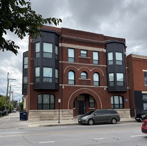 A grey van is parked in front of a red brick building with a black extension.