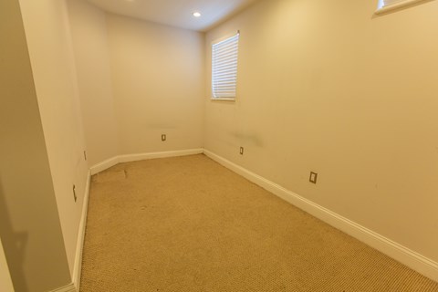A room with a carpeted floor and a window with blinds.