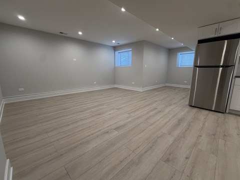 A spacious room with wooden flooring and a refrigerator on the right side.