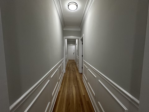 A long hallway with white walls and wood flooring.
