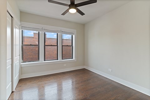 A room with a ceiling fan and a window with a view of a brick building.