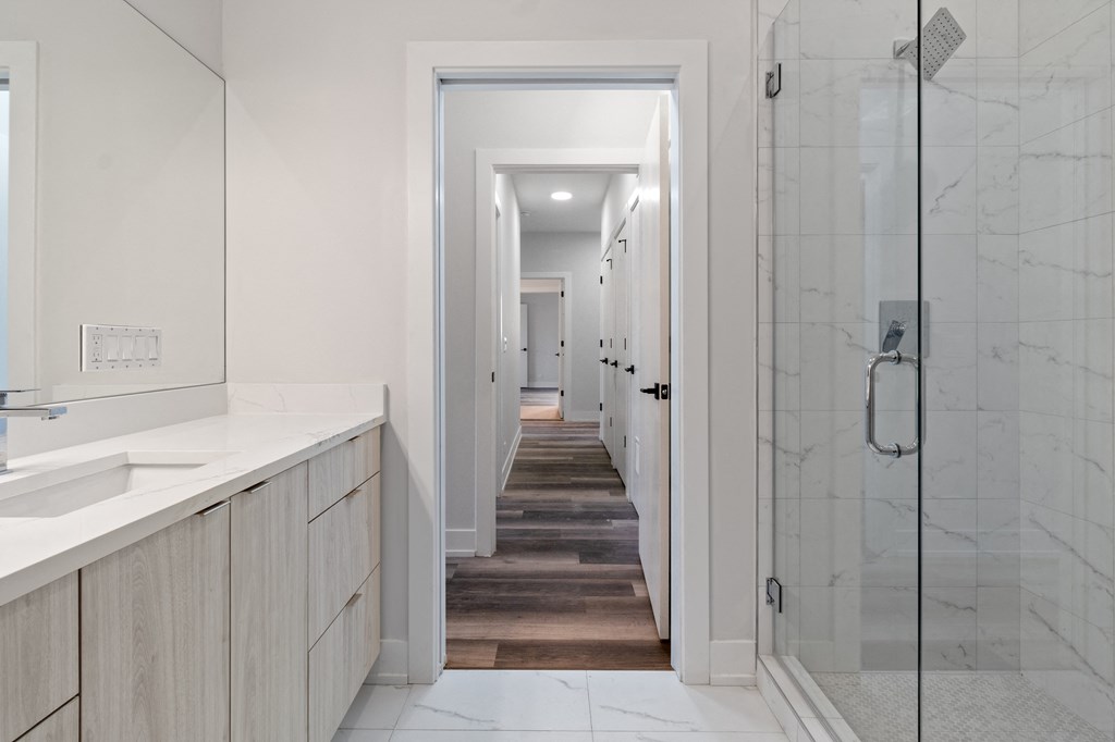 a long bathroom with a shower and a long hallway with a sink and a counter