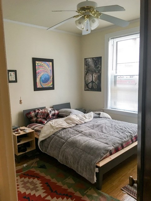 A bedroom with a bed, a ceiling fan, and two pictures on the wall.